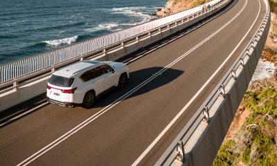 White Lexus LX drives across a highway road overlooking an ocean.