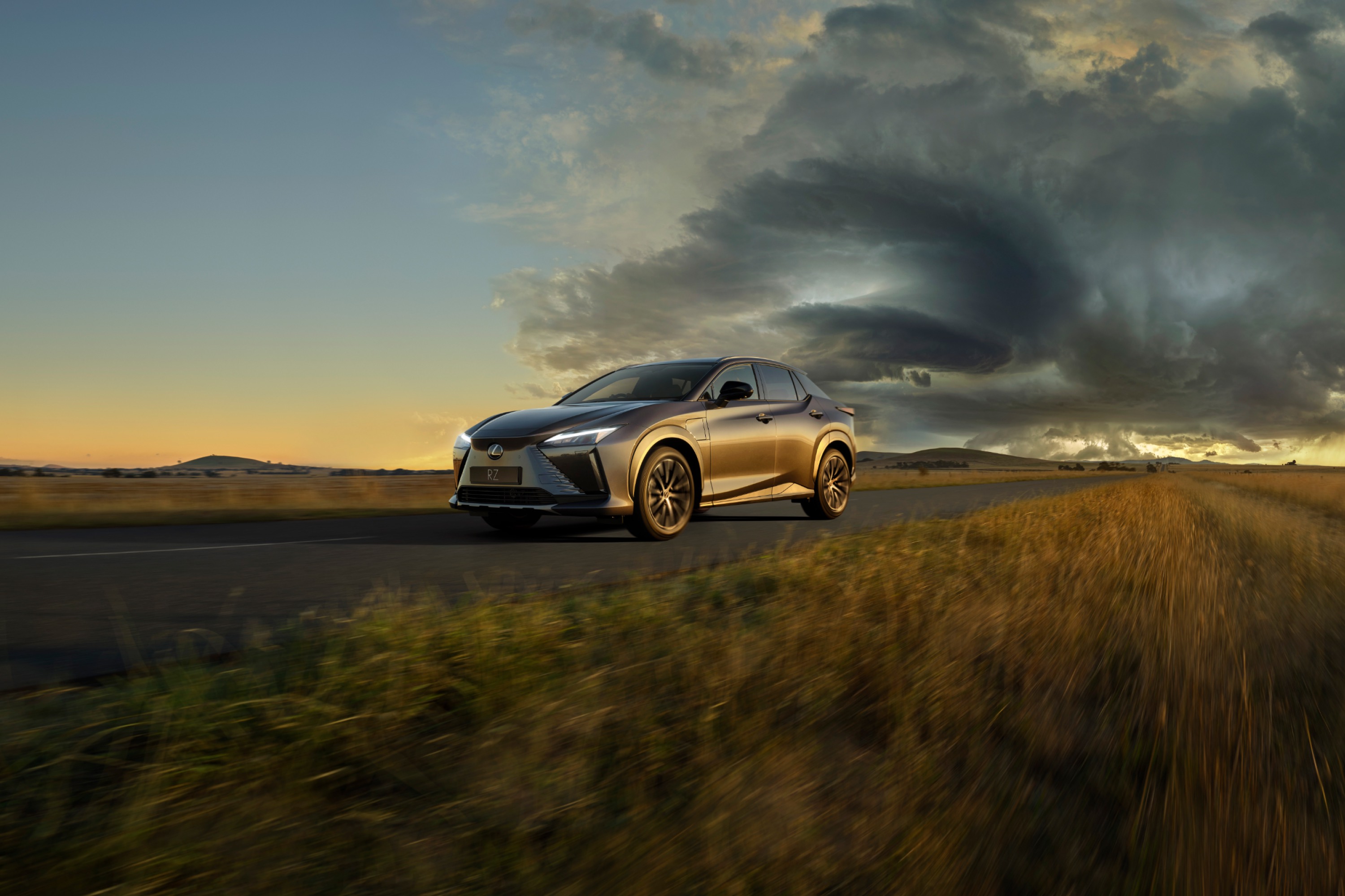 Lexus RZ drives on an Australian countryside road, away from a storm brewing in the far distance.