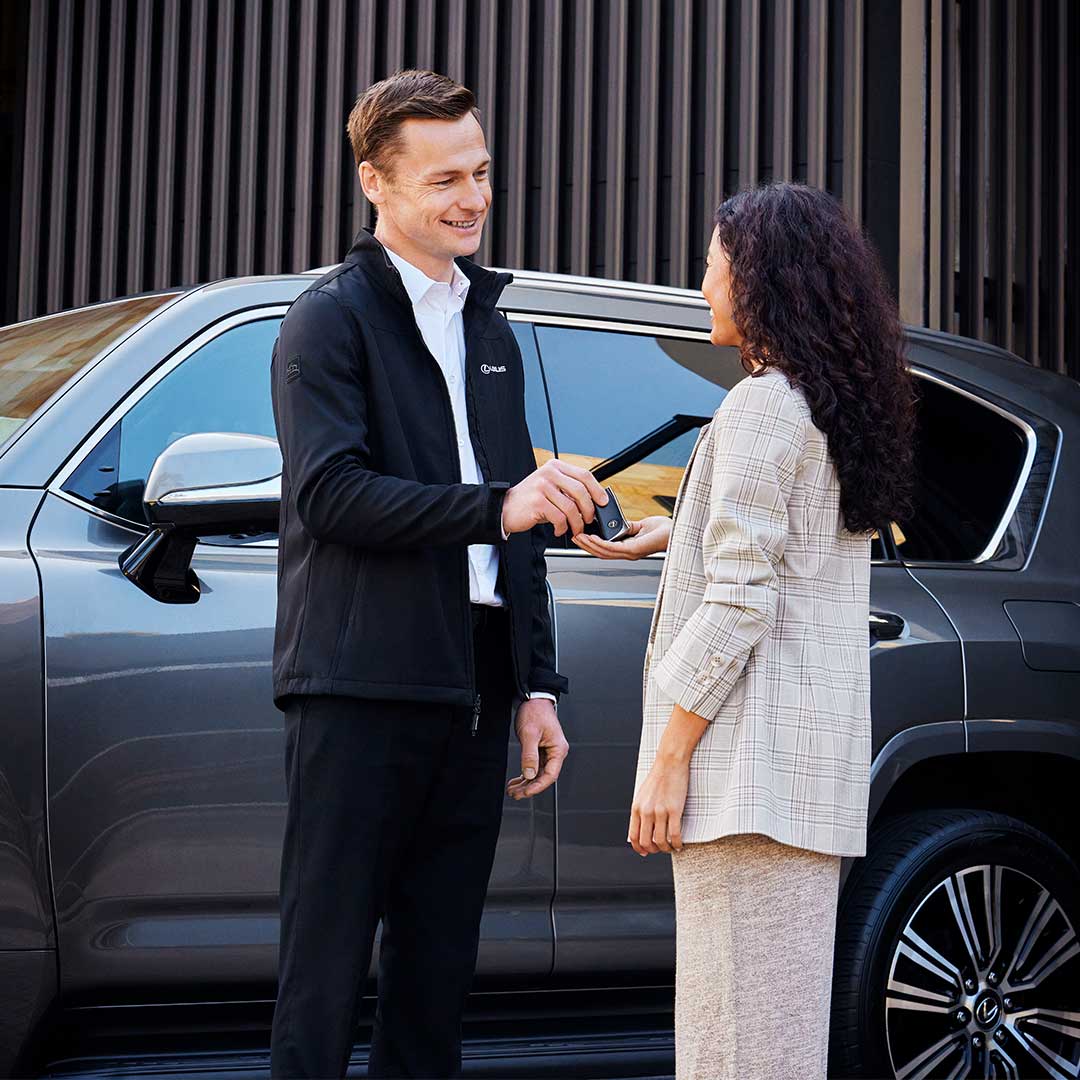 A man gives keys to a woman in front of a vehicle